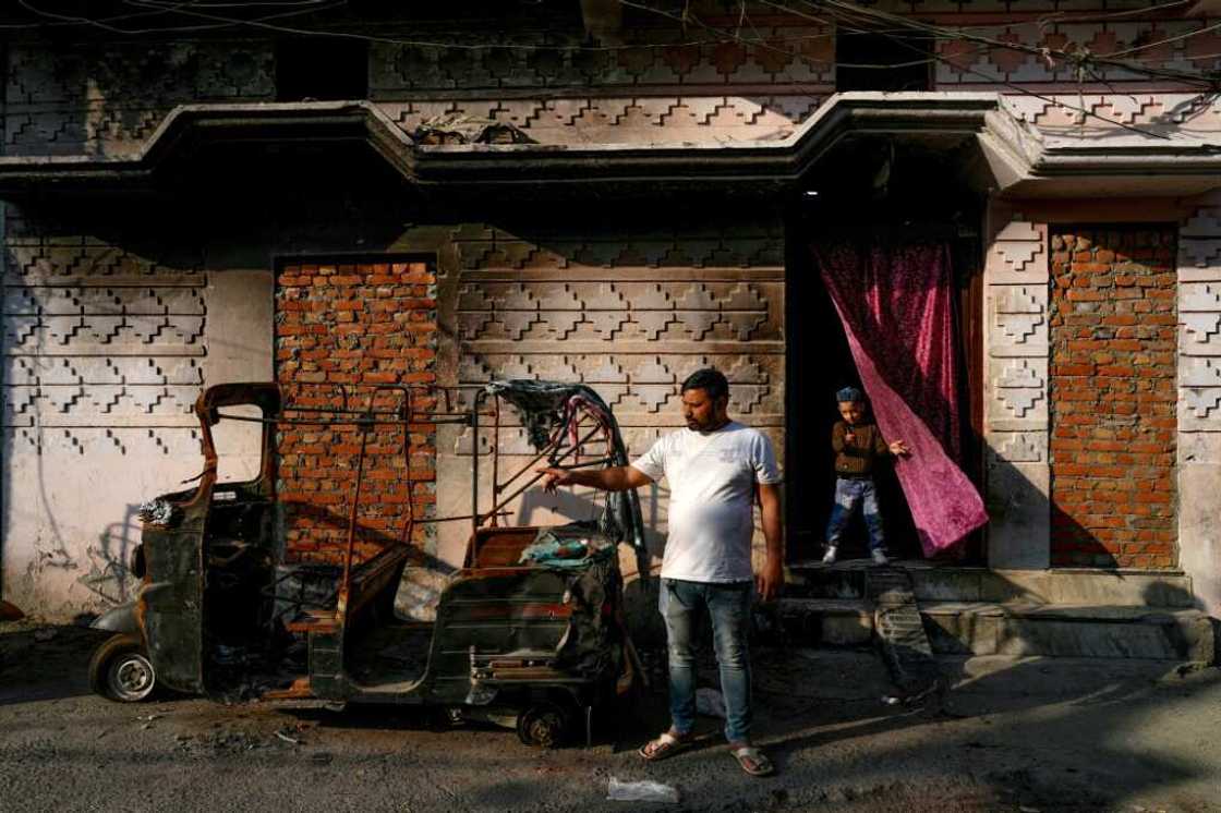 Parvez Qureshi stands beside an autorickshaw burnt during the violence in front of his house