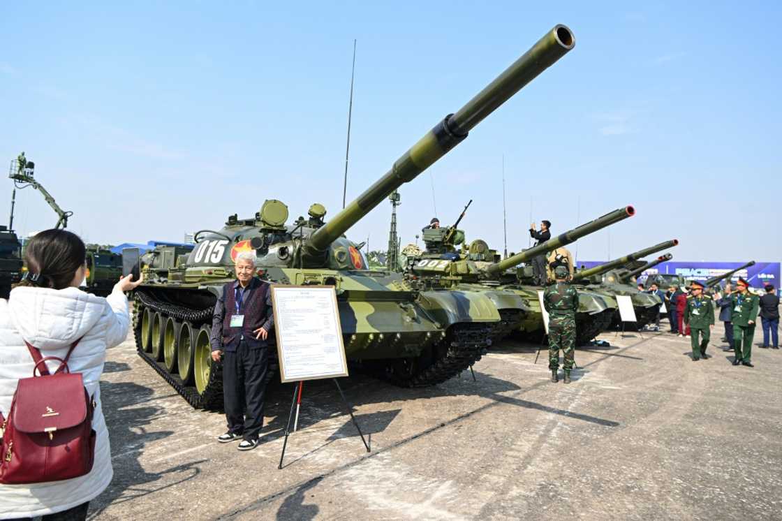 A man poses for a photo next to a tank during a defence expo in Hanoi