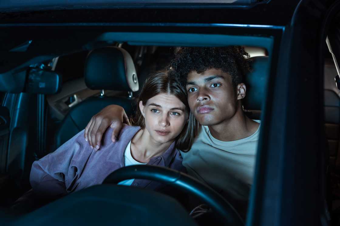 A young couple watching a movie while sitting together in a car in an open air cinema. A young couple watching a movie while sitting together in a car in an open air cinema.