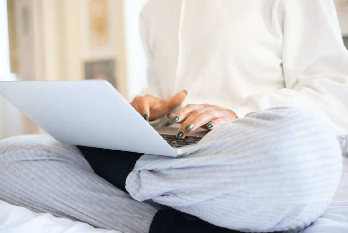 Close-up shot of a person in white using a laptop while sitting on a bed. Close-up shot of a person in white using a laptop while sitting on a bed.