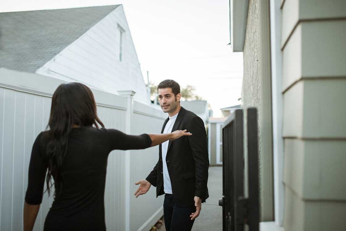A woman gestures for a man to stop during a tense conversation in a narrow outdoor passage.