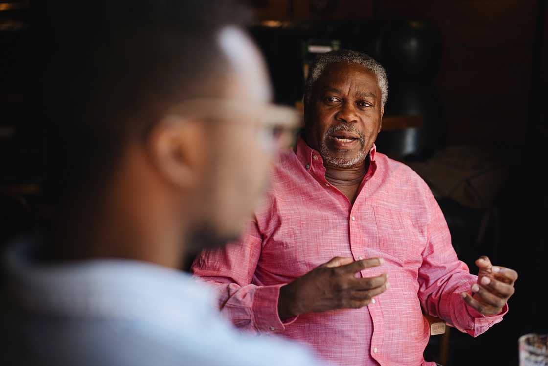 Older person gestures while speaking to someone indoors.