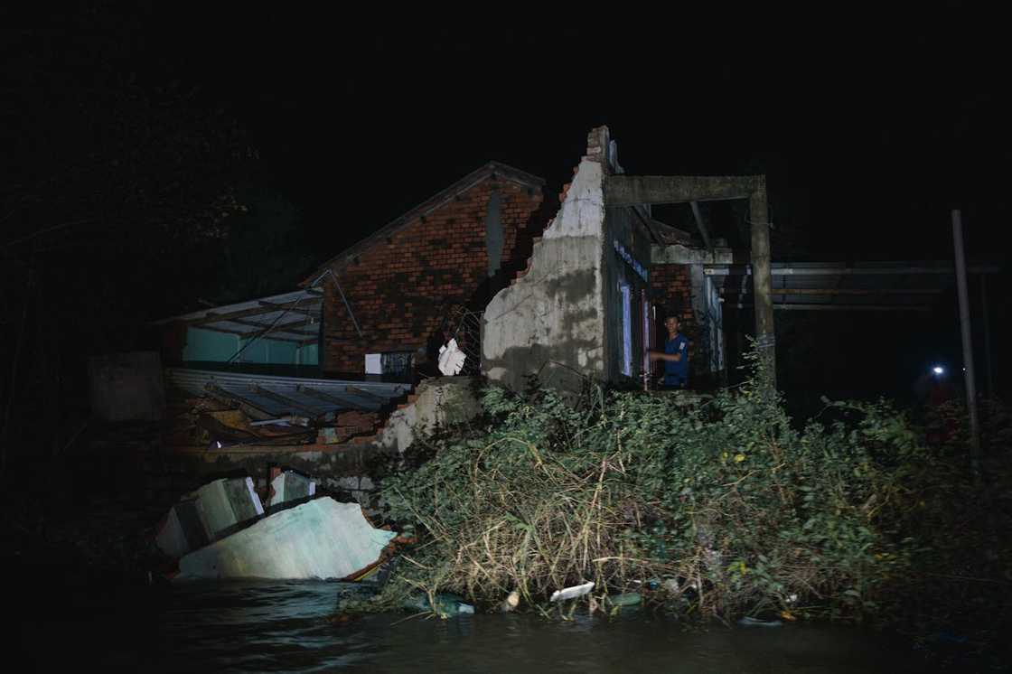 A partially collapsed house stands surrounded by floodwater.
