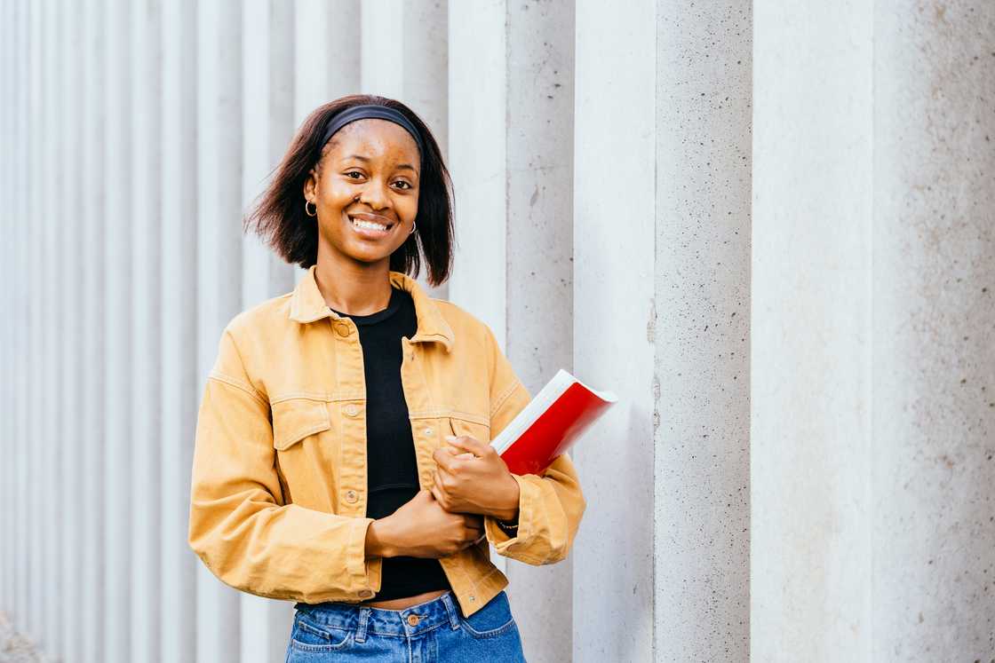 A young student university holding a red notebook.