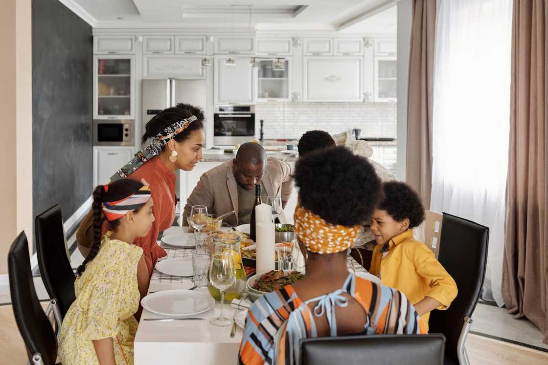 A family gathers around a dining table preparing to eat a meal.