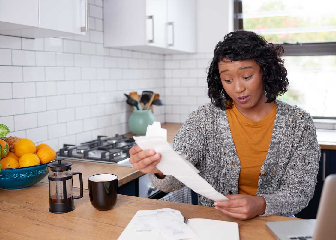 A person reviewing a long receipt at a kitchen counter.