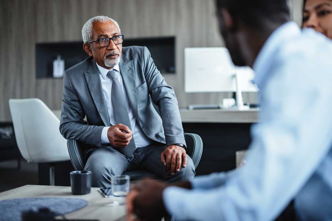An older man confronts a lawyer in a Lagos office under a ceiling fan.