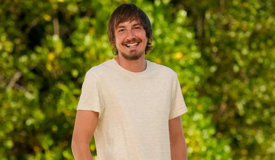 Kyle Ostwald poses standing against greenery