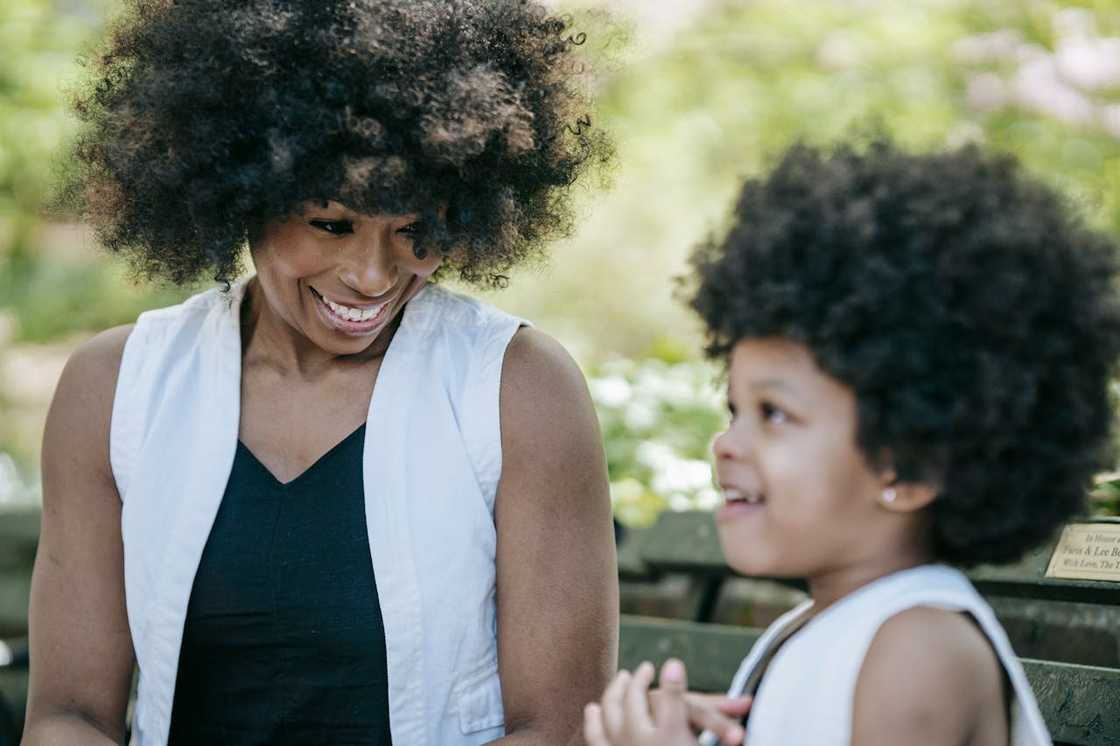 A woman and young child smiling together on a park bench.