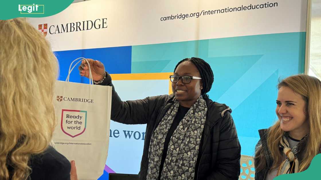 A lady giving a white bag with the Cambridge logo A lady giving a white bag with the Cambridge logo