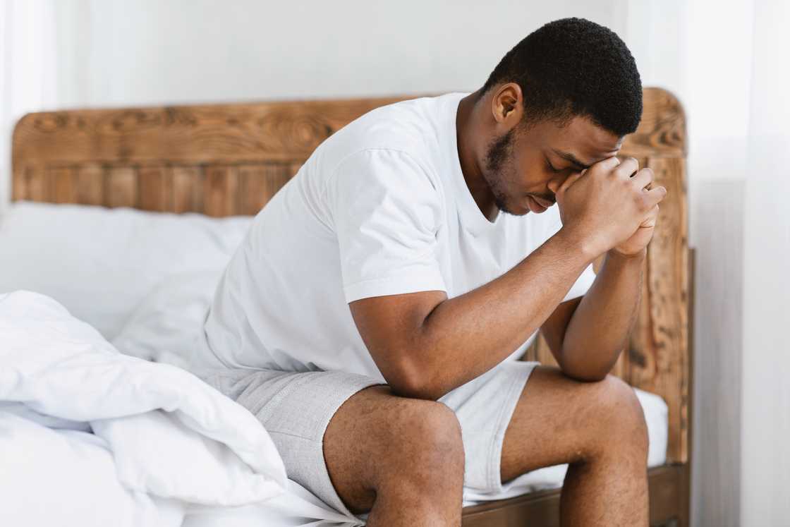 A person sitting on edge of bed in morning sunlight, head in hands. A person sitting on edge of bed in morning sunlight, head in hands.