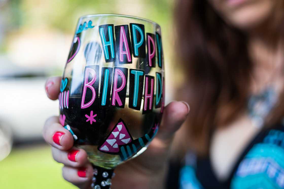 A lady holding a happy birthday wine glass with red wine.