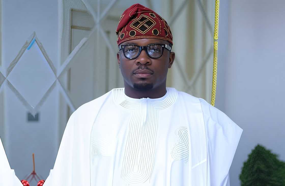 Sijibomi Ogundele poses standing in a white traditional Nigerian agbada, and a red patterned fila (cap) Sijibomi Ogundele poses standing in a white traditional Nigerian agbada, and a red patterned fila (cap)