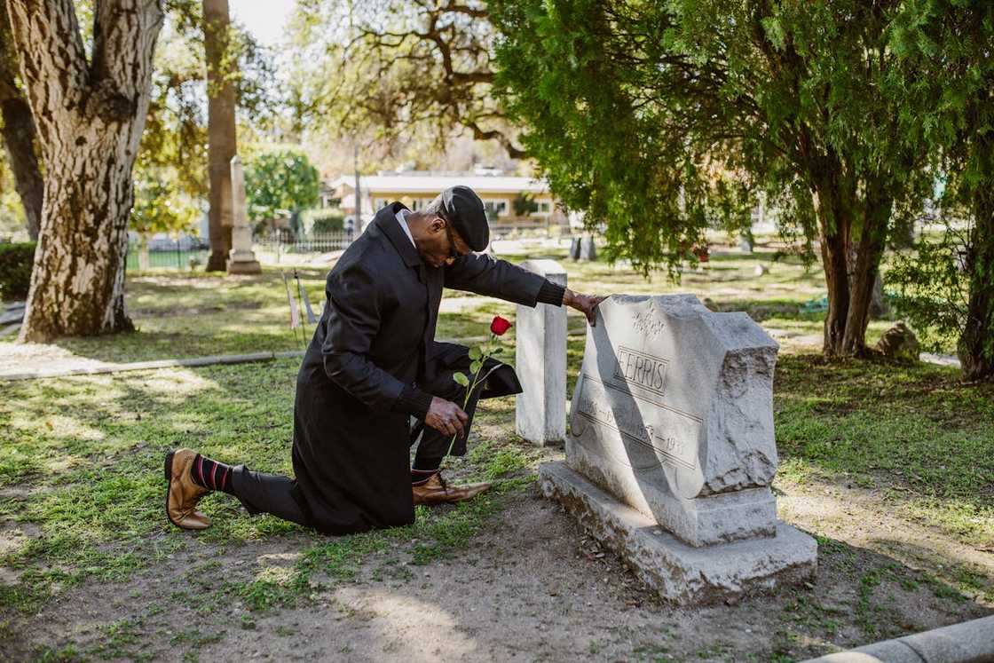 A man kneels at a gravestone, holding a single red rose. A man kneels at a gravestone, holding a single red rose.