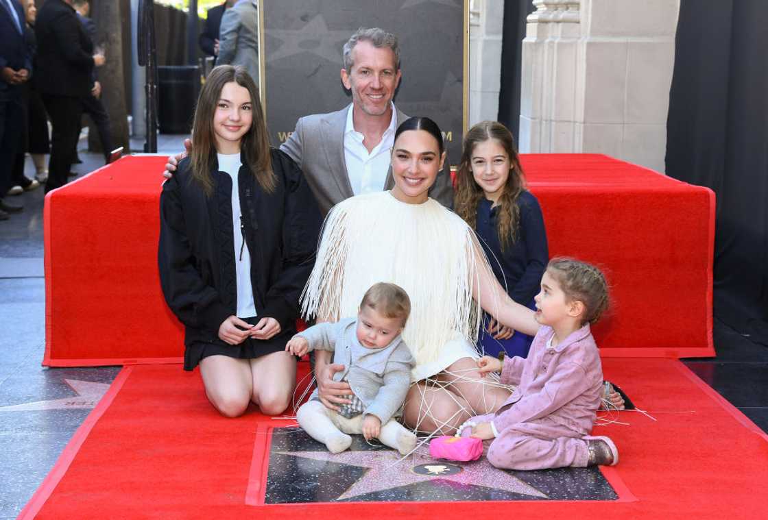 A woman in a fringed white dress kneels on a red carpet with a man and four children around a Walk of Fame star.