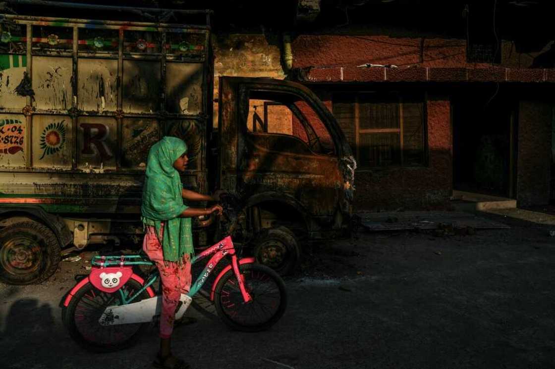 A girl rides a bicycle past a charred vehicle belonging to a local Muslim family burnt during the anti-Muslim riots in February A girl rides a bicycle past a charred vehicle belonging to a local Muslim family burnt during the anti-Muslim riots in February