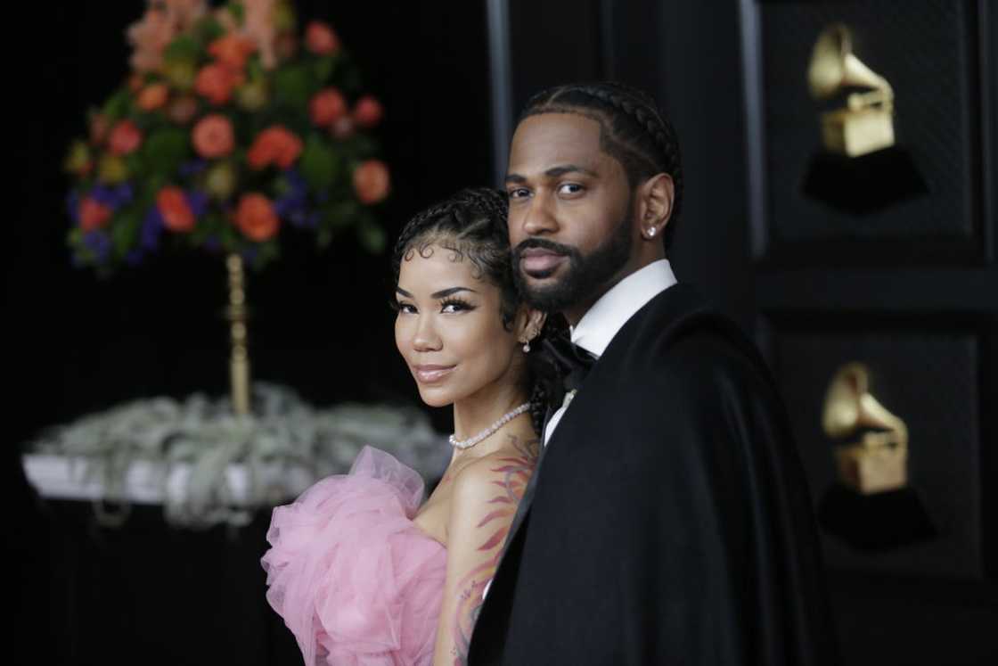 Jhené Aiko in a pink tulle dress stands close to Big Sean in a black tuxedo with a cape, Grammy trophies visible behind them.