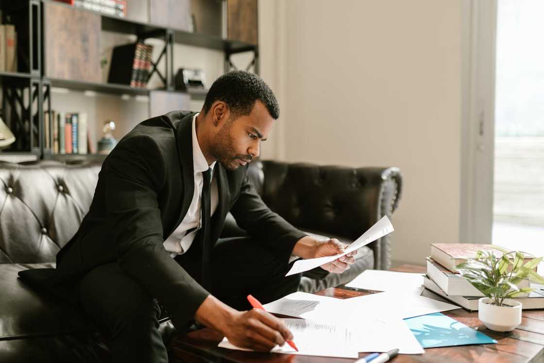 A businessman reviews documents and marking papers at a desk in an office.