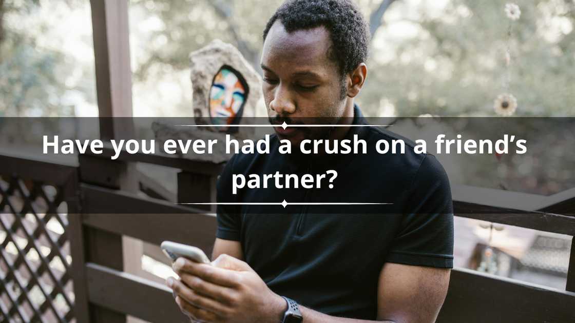 A man in a black tee is sitting on a wooden patio while texting on a white smartphone A man in a black tee is sitting on a wooden patio while texting on a white smartphone