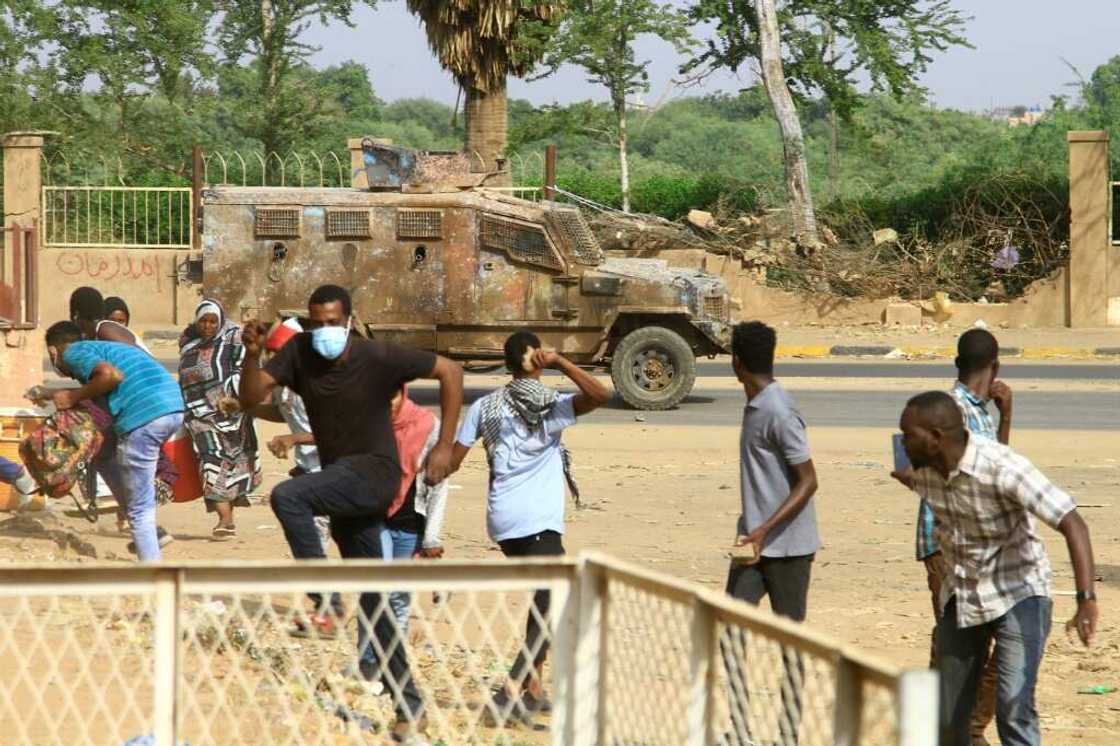 Sudanese anti-coup demonstrators duck for cover as a police vehicle fires tear gas in a street in the capital's twin city of Omdurman