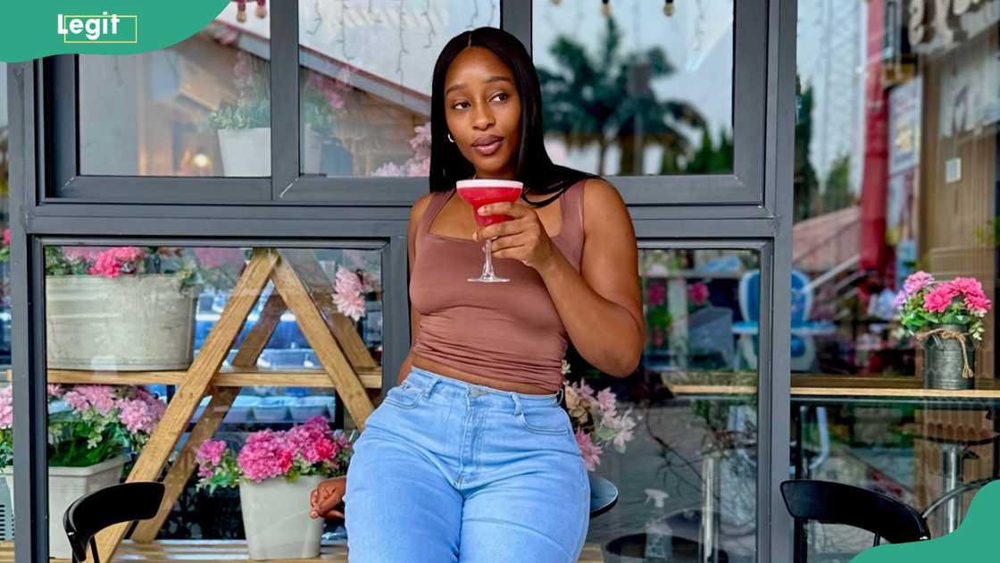 Sheba holds a red drink while seated outside a café
