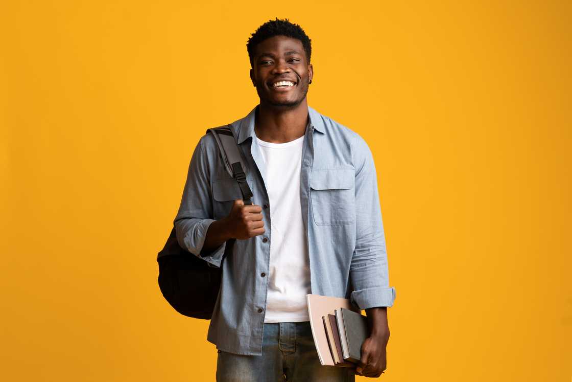 A student in casual posing with books and notepads on a yellow studio background.