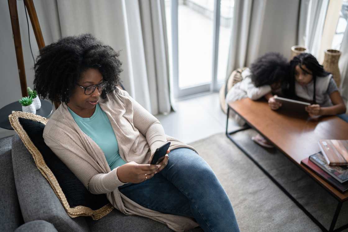 A mother scrolls her phone while children sit silently nearby.
