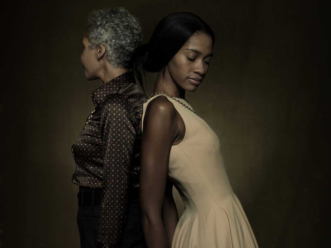 Two people stand back-to-back with eyes closed against a dark background.