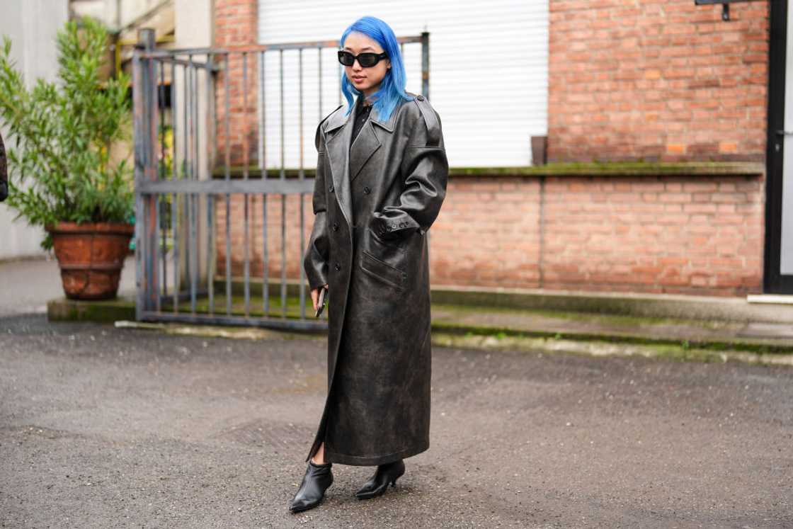 Margaret Zhang wears sunglasses, a black leather trench long coat, and kitten heels