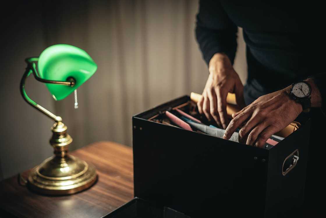 A person sorts through files in a storage box beside a lamp.