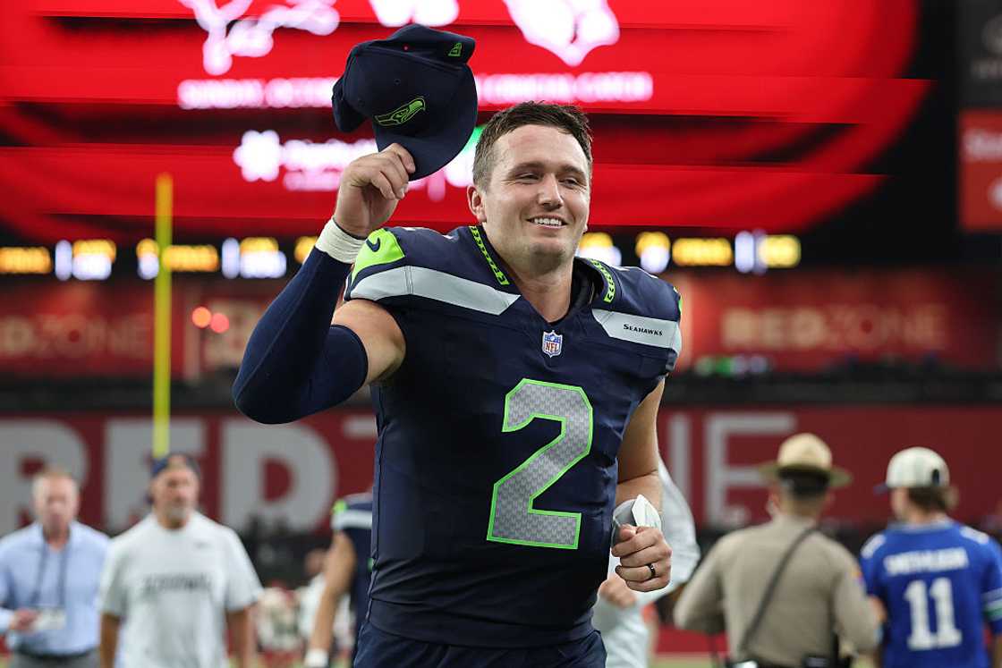 A football player in a navy Seahawks jersey numbered 2 holds up his cap and smiles. A football player in a navy Seahawks jersey numbered 2 holds up his cap and smiles.