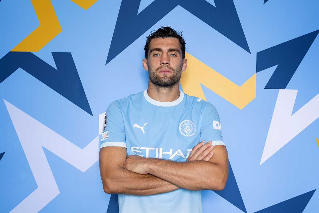 Mateo Kovačić, in the sky-blue Manchester City home kit, poses with arms folded against a blue patterned backdrop at the club's Champions League 2026/27 portrait session. Mateo Kovačić, in the sky-blue Manchester City home kit, poses with arms folded against a blue patterned backdrop at the club's Champions League 2026/27 portrait session.