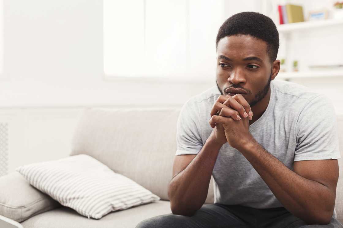 A man with hands clasped thinking while sitting on couch A man with hands clasped thinking while sitting on couch
