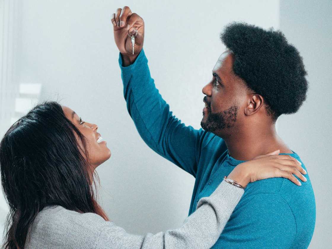 Couple smiling as one person holds up a set of keys indoors. Couple smiling as one person holds up a set of keys indoors.