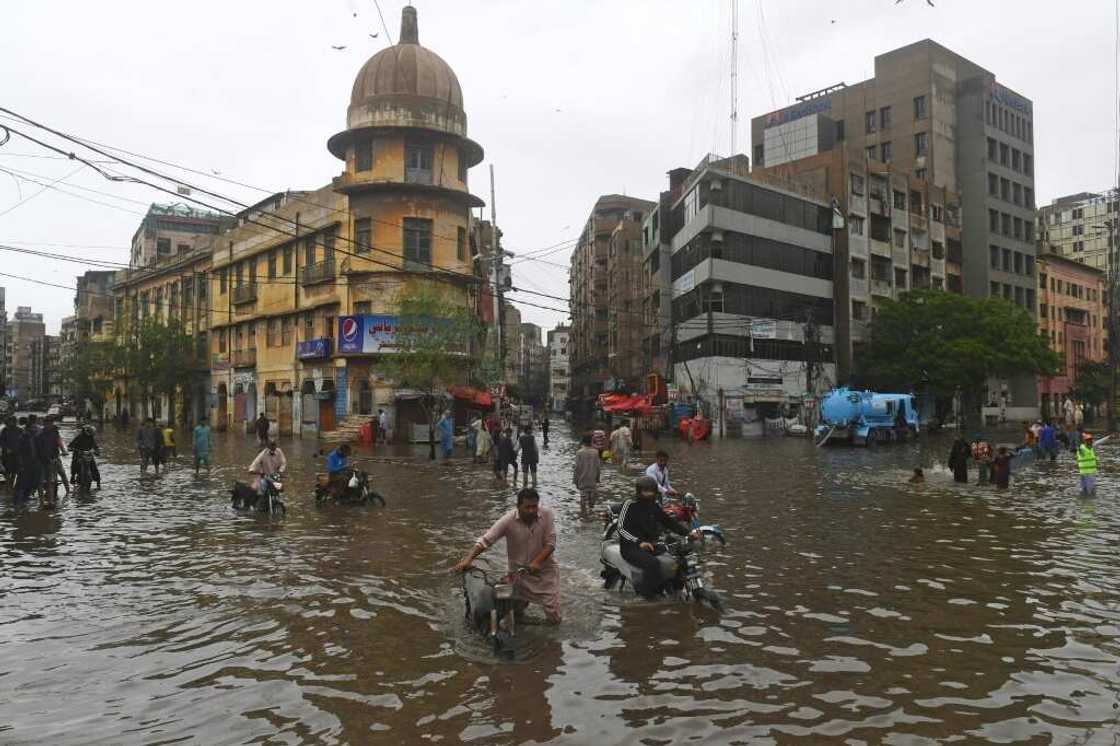 Motorcyclists push their vehicles through a flooded street in Pakistan's port city of Karachi