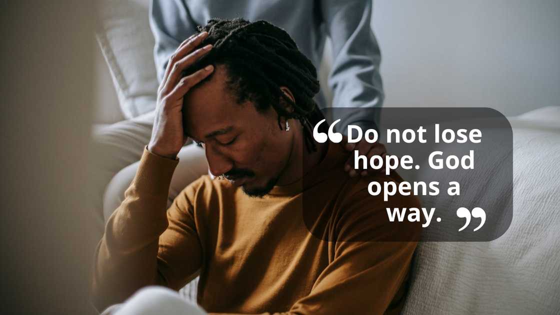 A distressed man sits while someone comforts him.