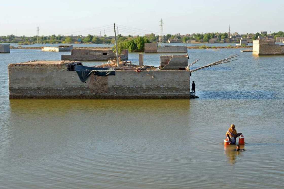 A woman wades through the flood waters to get drinking water in Dera Allah Yar, Pakistan; fossil fuel usage is a major contributor to climate change