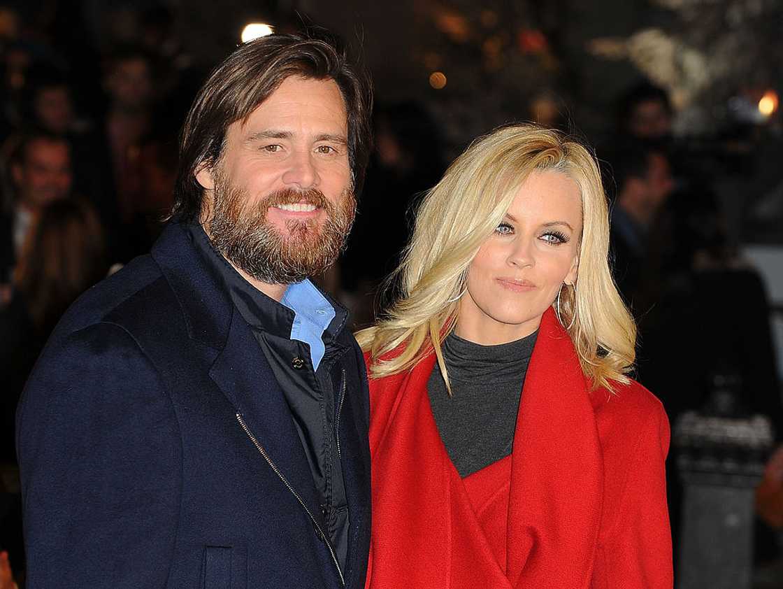 Jim Carrey in a navy coat stands with Jenny McCarthy in a red wrap coat at a night event. Jim Carrey in a navy coat stands with Jenny McCarthy in a red wrap coat at a night event.