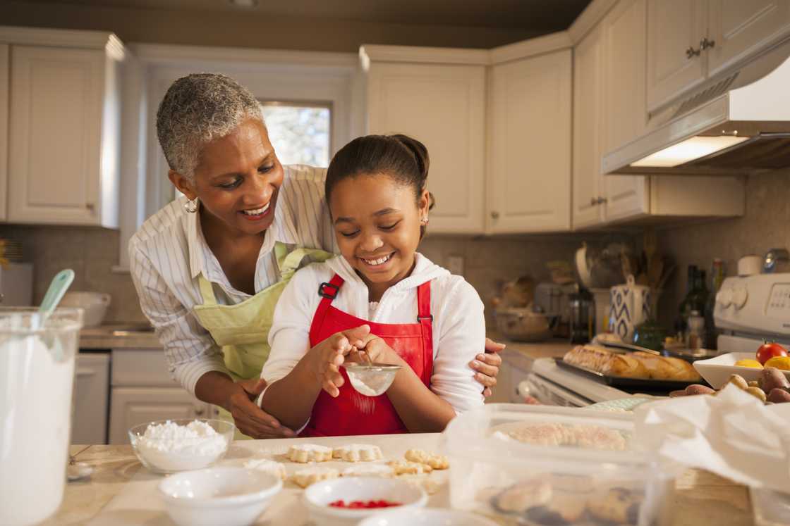 Older woman embraces young girl while baking in kitchen. Older woman embraces young girl while baking in kitchen.