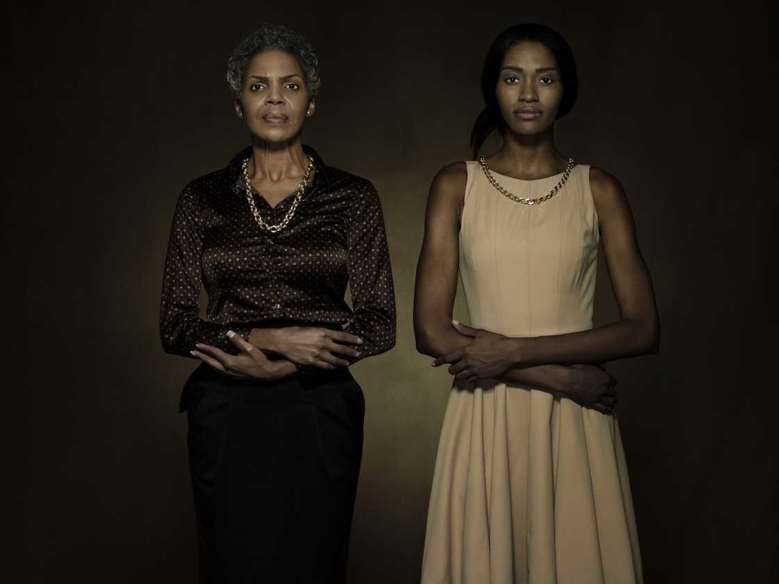 Two individuals stand side by side with arms crossed against a dark background.