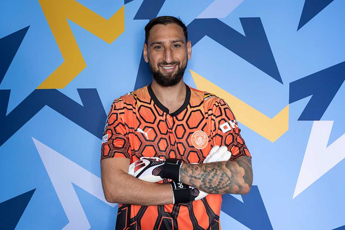 Gianluigi Donnarumma, in an orange Manchester City goalkeeper kit, poses against a blue patterned backdrop. Gianluigi Donnarumma, in an orange Manchester City goalkeeper kit, poses against a blue patterned backdrop.