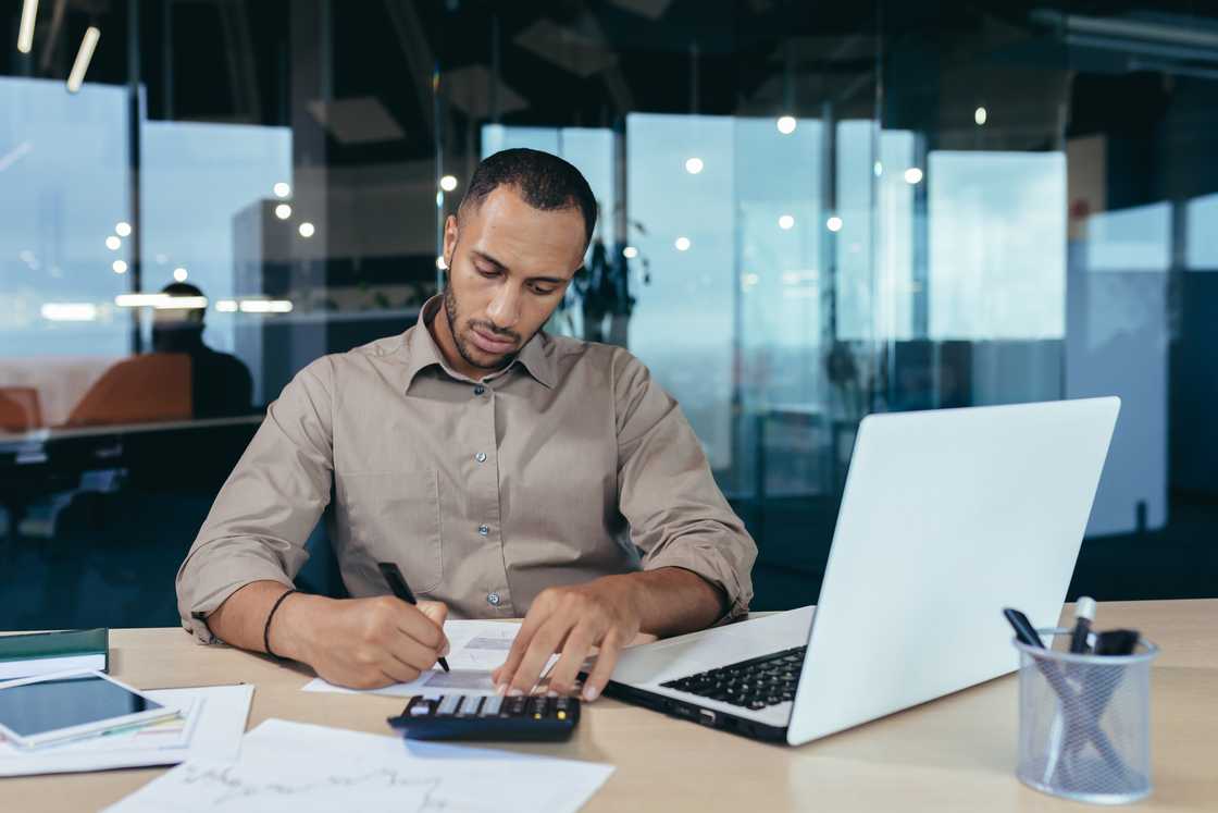 An accountant working in office at desk with laptop and documents.
