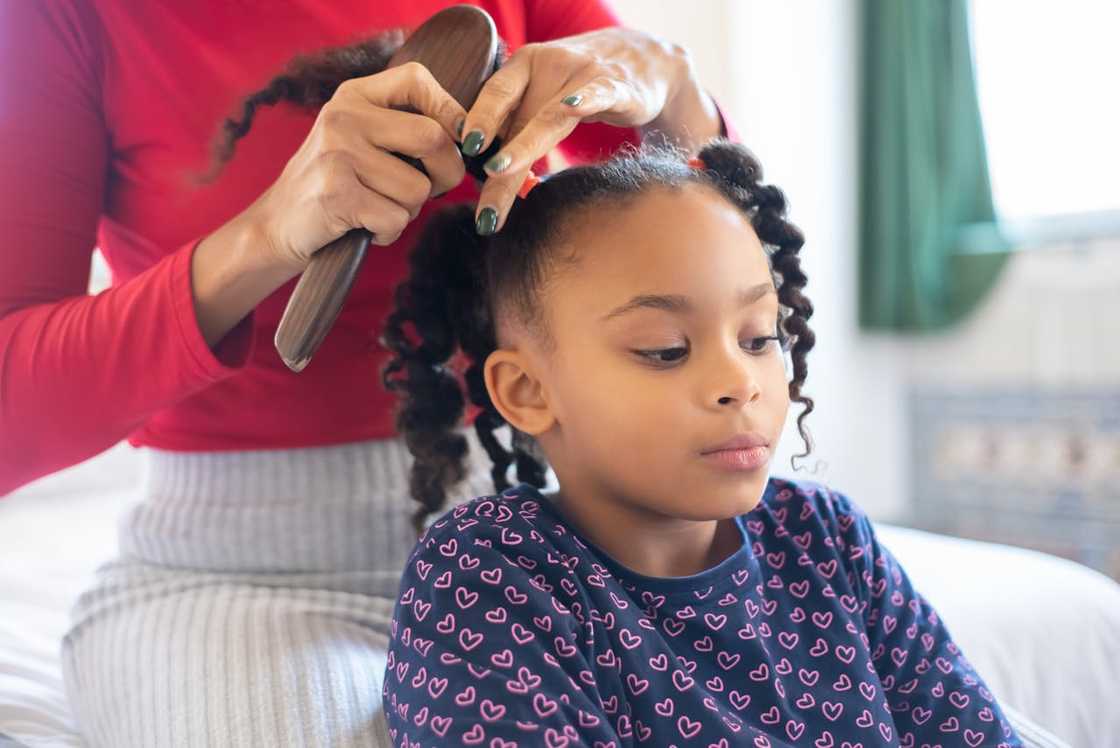 An adult styling a child’s hair while the child sits calmly. An adult styling a child’s hair while the child sits calmly.