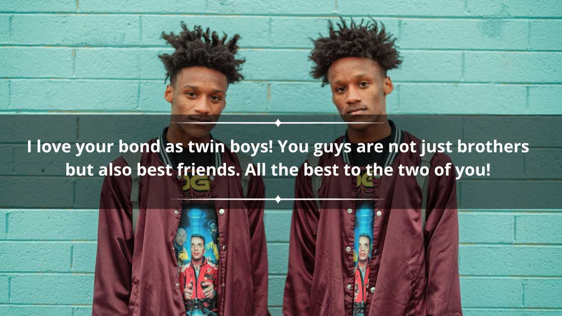 Twin boys in matching maroon jackets and colourful tees are standing in front of a blue wall