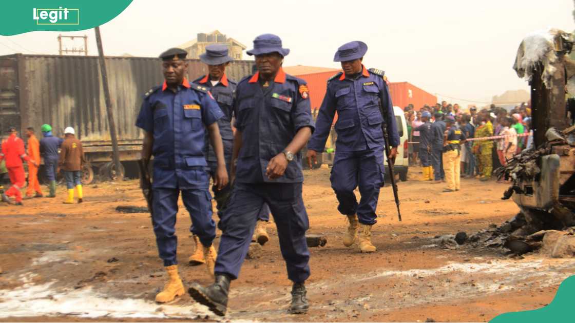Officers of the Nigeria Security and Civil Defence Corps in dark blue uniforms and caps walking along a road in Abule-Egba, Lagos, 2020