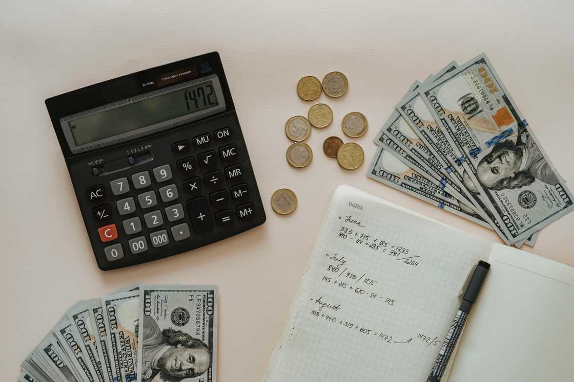 A bunch of dollar notes and coins next to a calculator and notebook on a flat surface A bunch of dollar notes and coins next to a calculator and notebook on a flat surface