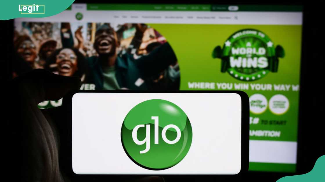 A phone showing the green Glo logo is held up against a blurred Glo website homepage in the background.