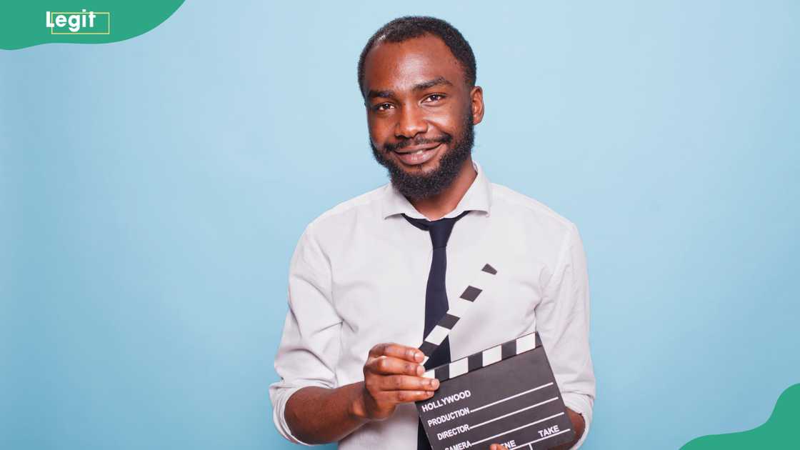 A young filmmaker grasping a clapper standing against a blue background A young filmmaker grasping a clapper standing against a blue background