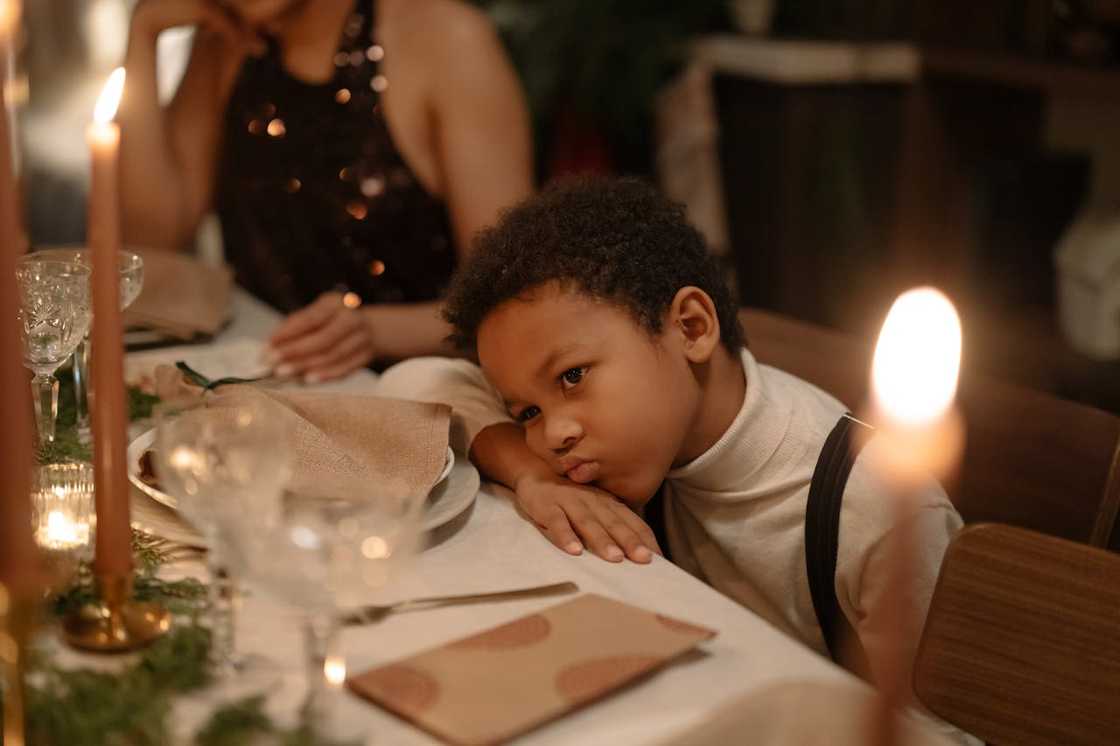 A young boy rests his head on a table during a candlelit dinner. A young boy rests his head on a table during a candlelit dinner.