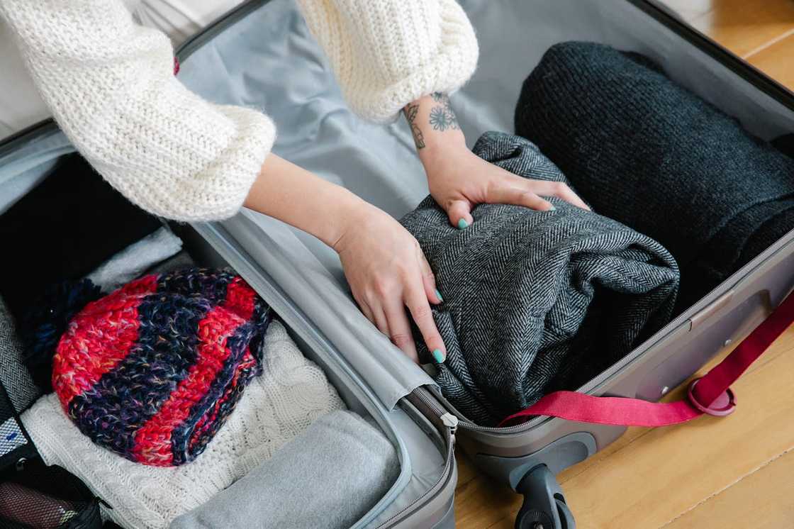 Hands packing folded clothes into an open suitcase.